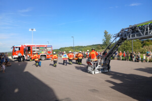 Feuerwehrleute tragen eine verletzte Person vom Drehleiterfahrzeug in Richtung des Löschfahrzeugs.