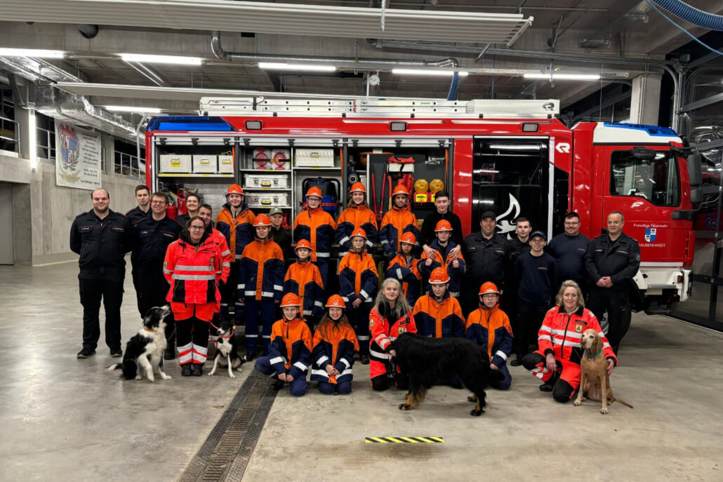 Ein Gruppenbild der Jugendlichen, ihrer Betreuer sowie der Rettungshunde und Hundeführer vor einem Feuerwehrfahrzeug.